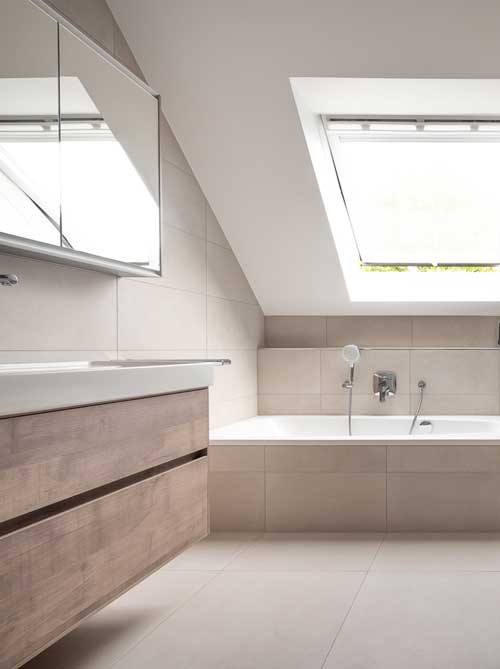 Minimalistisches Bad mit Badewanne unter der Schräge, großem Dachfenster und Waschtisch in Holzoptik