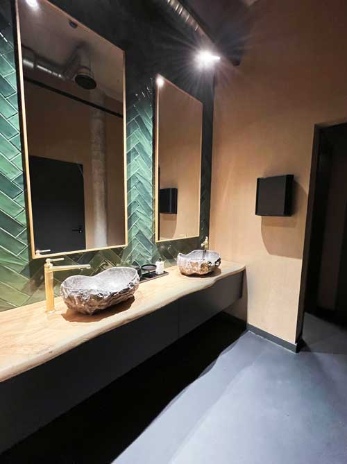 Ausdrucksstarkes Designbad mit Naturstein-Waschbecken, grün gefliester Rückwand und stimmungsvoller Beleuchtung