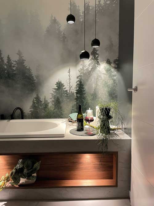 Atmosphärisches Bad mit Waldbild, freistehender Badewanne und stimmungsvoller Lichtinszenierung