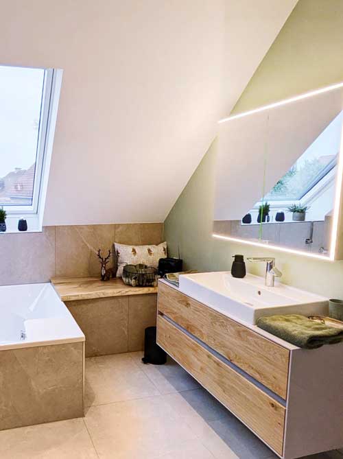 Helles Dachgeschossbad mit grüner Wandfarbe, Holzwaschtisch und gemütlicher Fenstersitzban
