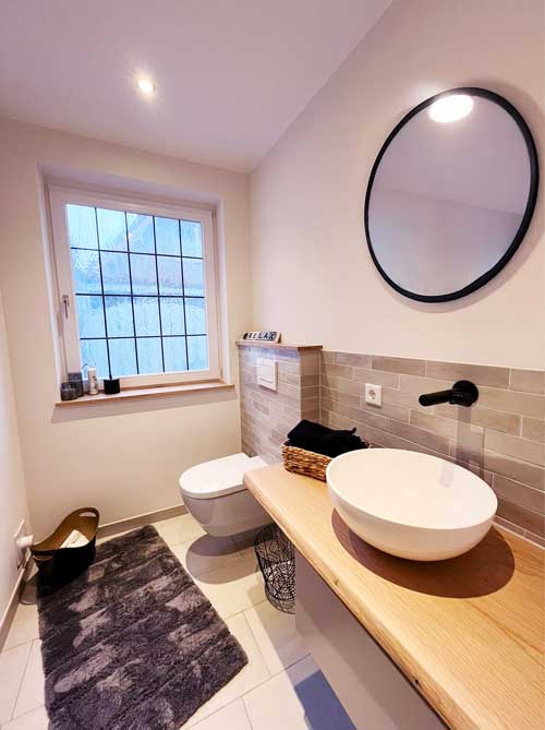 Modernes Gäste-WC mit rundem Spiegel, Aufsatzwaschbecken und hellem Tageslichtfenster