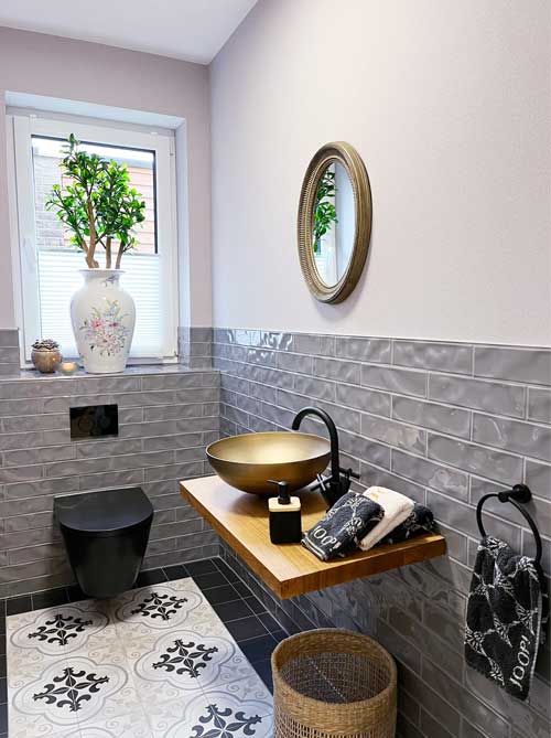 Stilvolles WC mit schwarzem WC-Keramik, goldfarbenem Aufsatzwaschbecken und gemustertem Fliesenboden