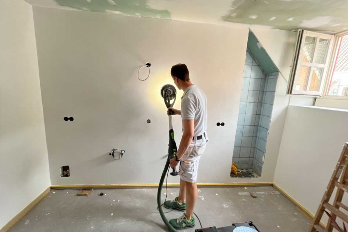 Renovierungsphase: Ein Handwerker schleift frisch verputzte Wände.