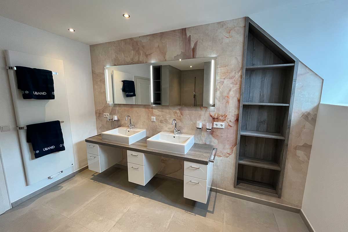 Modernisiertes Badezimmer mit zwei eckigen Waschbecken, großem LED-Spiegel, dekorativer Wandverkleidung und Regal in Dachschräge.