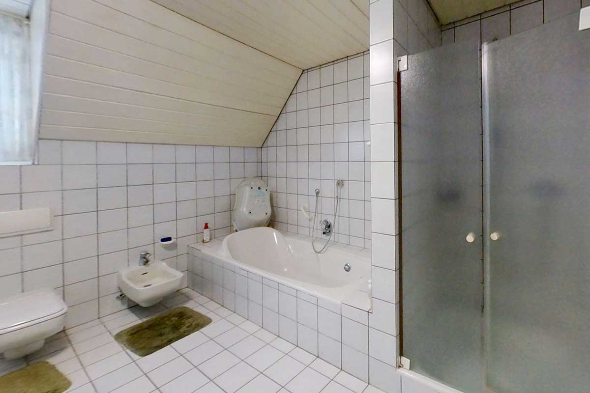 Altbestand: Badezimmer mit Fliesen aus den 90er-Jahren, Badewanne unter der Schräge, Bidet, Toilette und Duschkabine.