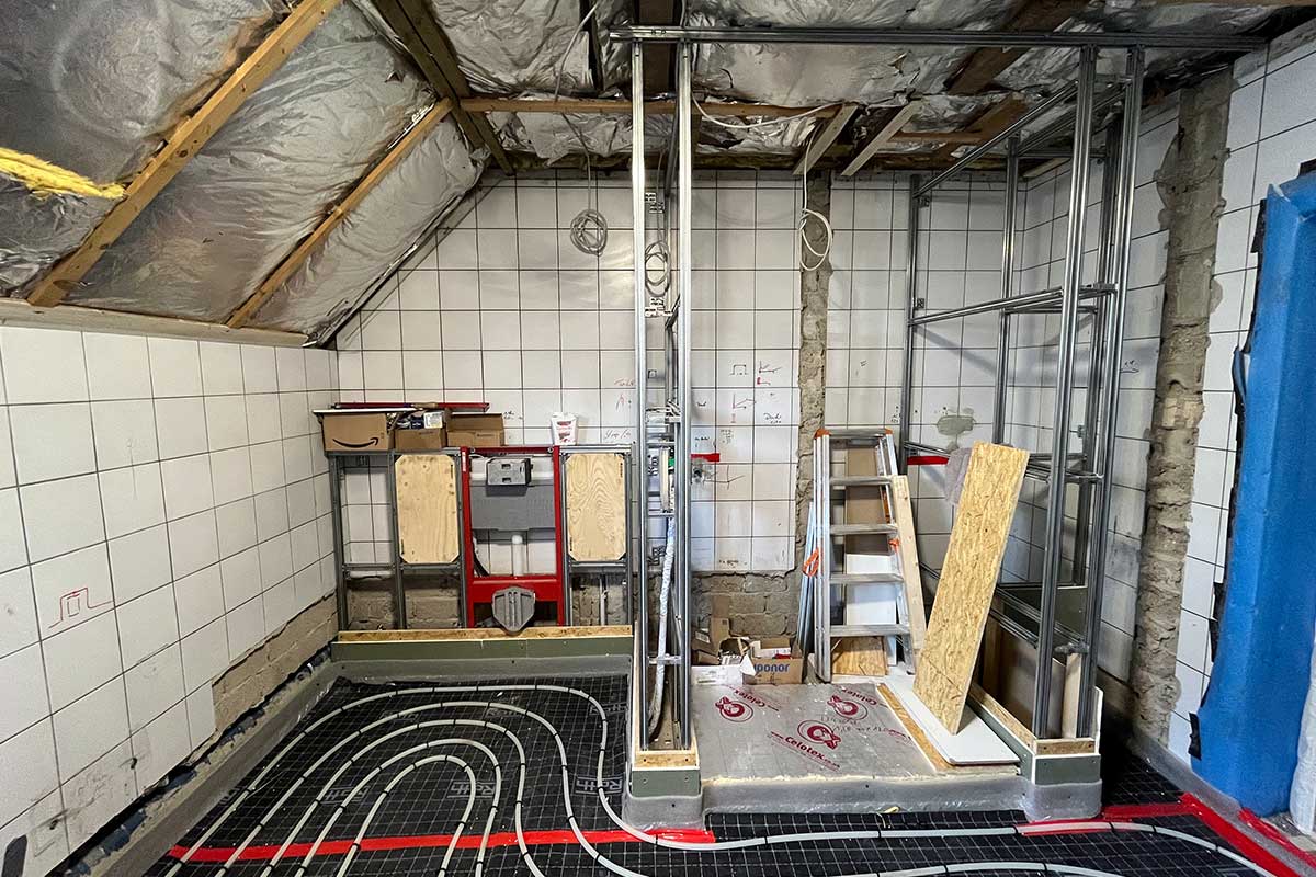 Rückbau und Neuaufbau: freigelegte Installation, Unterkonstruktion für Vorwand, sichtbare Dachschräge und Fußbodenheizung.