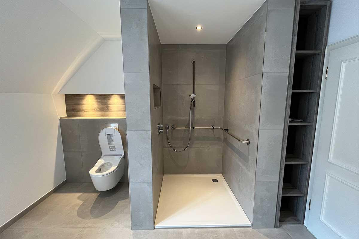 Endergebnis: barrierefreie Dusche mit Haltegriffen, Nische und Duschsitz, daneben wandhängendes Dusch-WC unter beleuchteter Holzverkleidung.