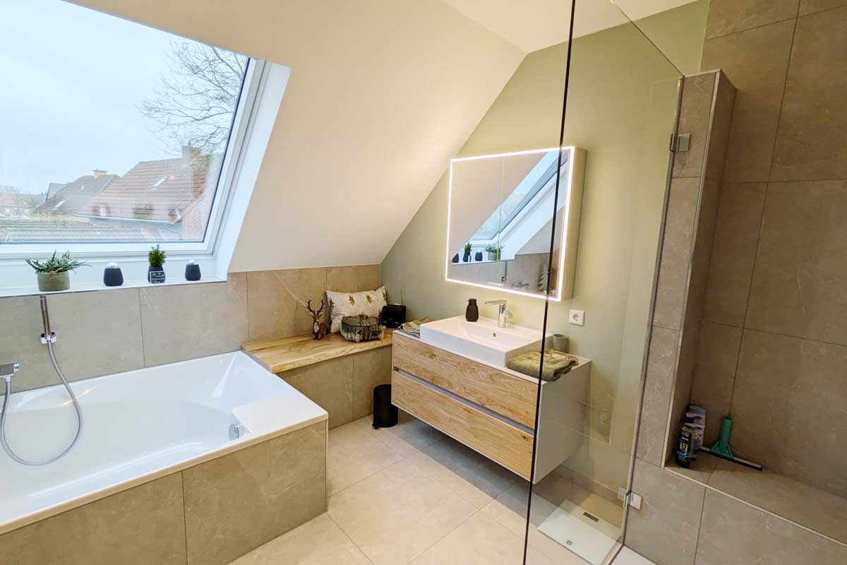 Modernes Bad mit Badewanne unter einem großen Dachfenster, daneben Sitzbank und Waschtisch mit beleuchtetem Spiegel.