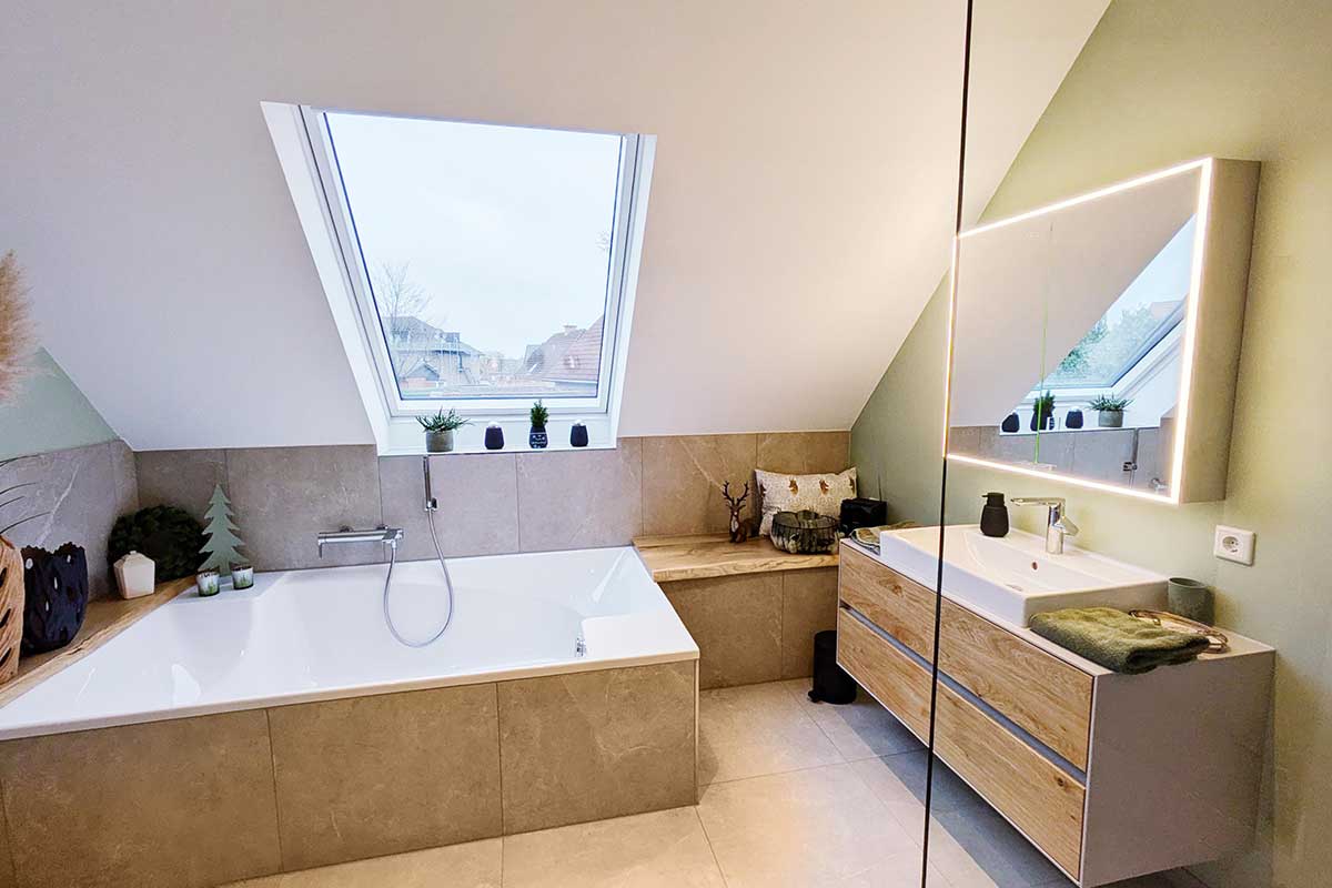 Blick auf Badewanne, Sitzbank mit Kissen und daneben der Waschtisch mit großem Spiegel und Holzschubladen.