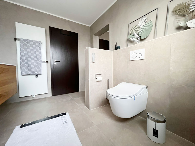 Modernes Badezimmer mit wandhängendem WC, Natursteinoptik-Fliesen und stilvollem Designheizkörper.