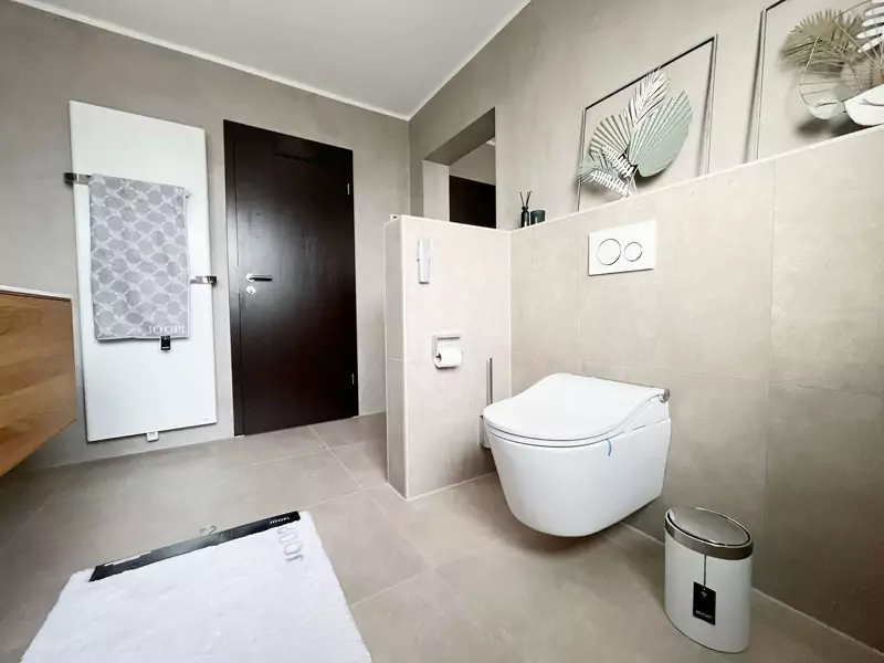 Modernes Badezimmer mit wandhängendem WC, Natursteinoptik-Fliesen und stilvollem Designheizkörper.