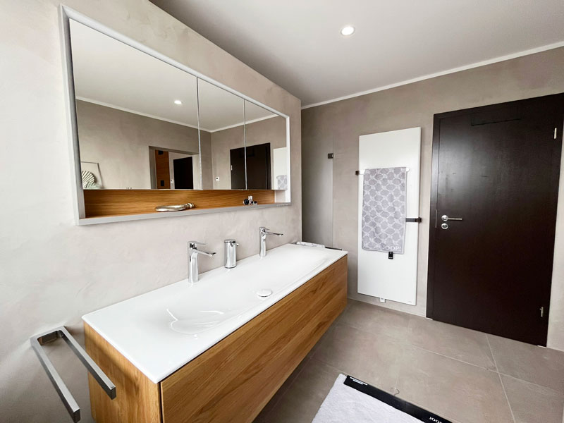 Großer Doppelwaschtisch mit Holzunterschrank, breitem Spiegel und eleganten Armaturen in einem modernen Designbad.