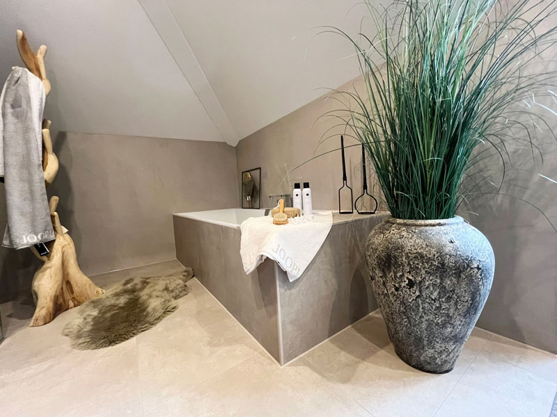 Freistehende Badewanne in Natursteinoptik mit dekorativen Accessoires und stilvoller Spa-Atmosphäre.