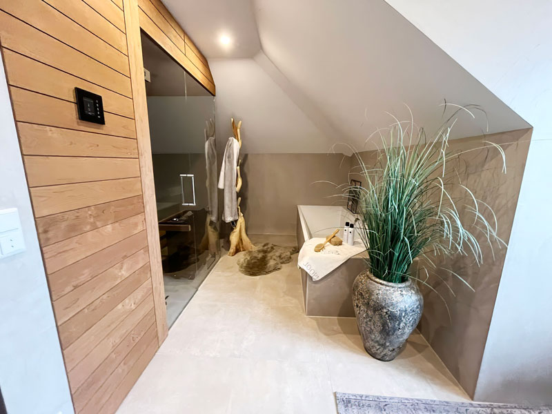 Großzügiger Wellnessbereich mit Sauna, Badewanne und dekorativen Pflanzen im modernen Designbad.