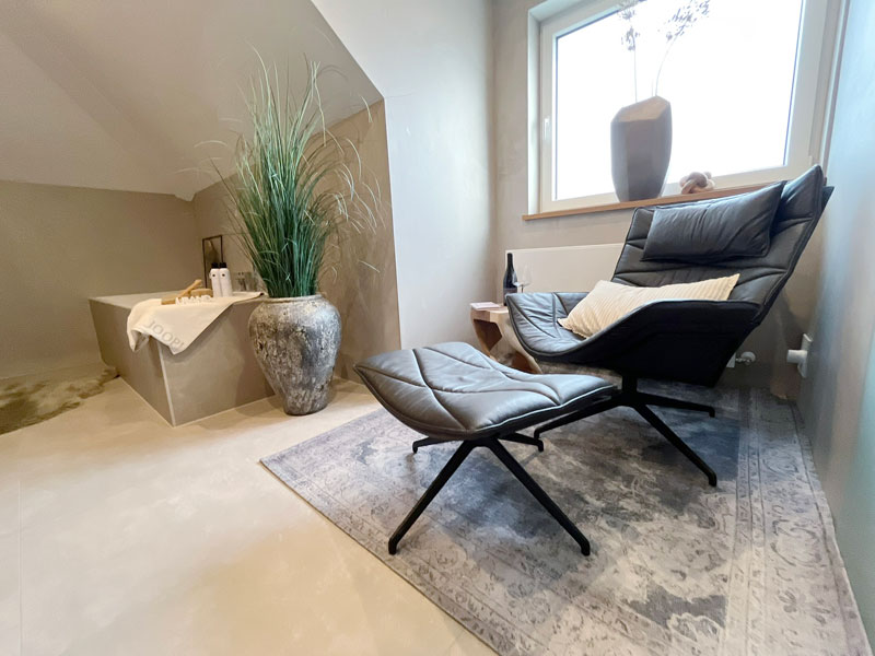 Gemütlicher Relaxbereich mit Lounge-Sessel neben Sauna und Badewanne im privaten Wellnessbad.