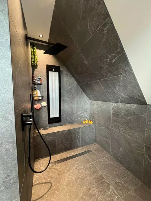 Großzügige Walk-in Dusche mit Natursteinfliesen, Sitzbank und schwarzer Regendusche unter Dachschräge
