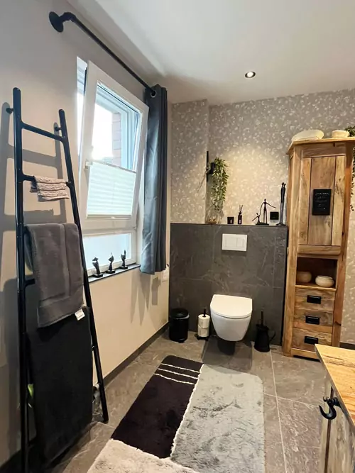 Badezimmer mit rustikalem Holzschrank, Leiter-Handtuchhalter und Natursteinfliesen im skandinavischen Stil