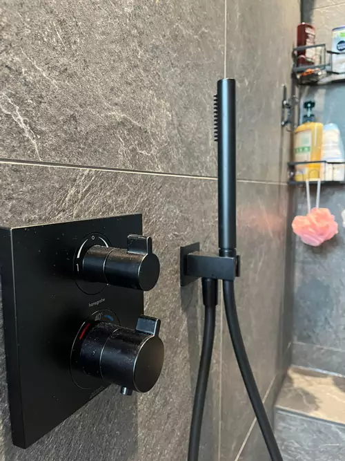 Detailaufnahme schwarzer Duscharmaturen und Handbrause an Natursteinwand in moderner Dusche